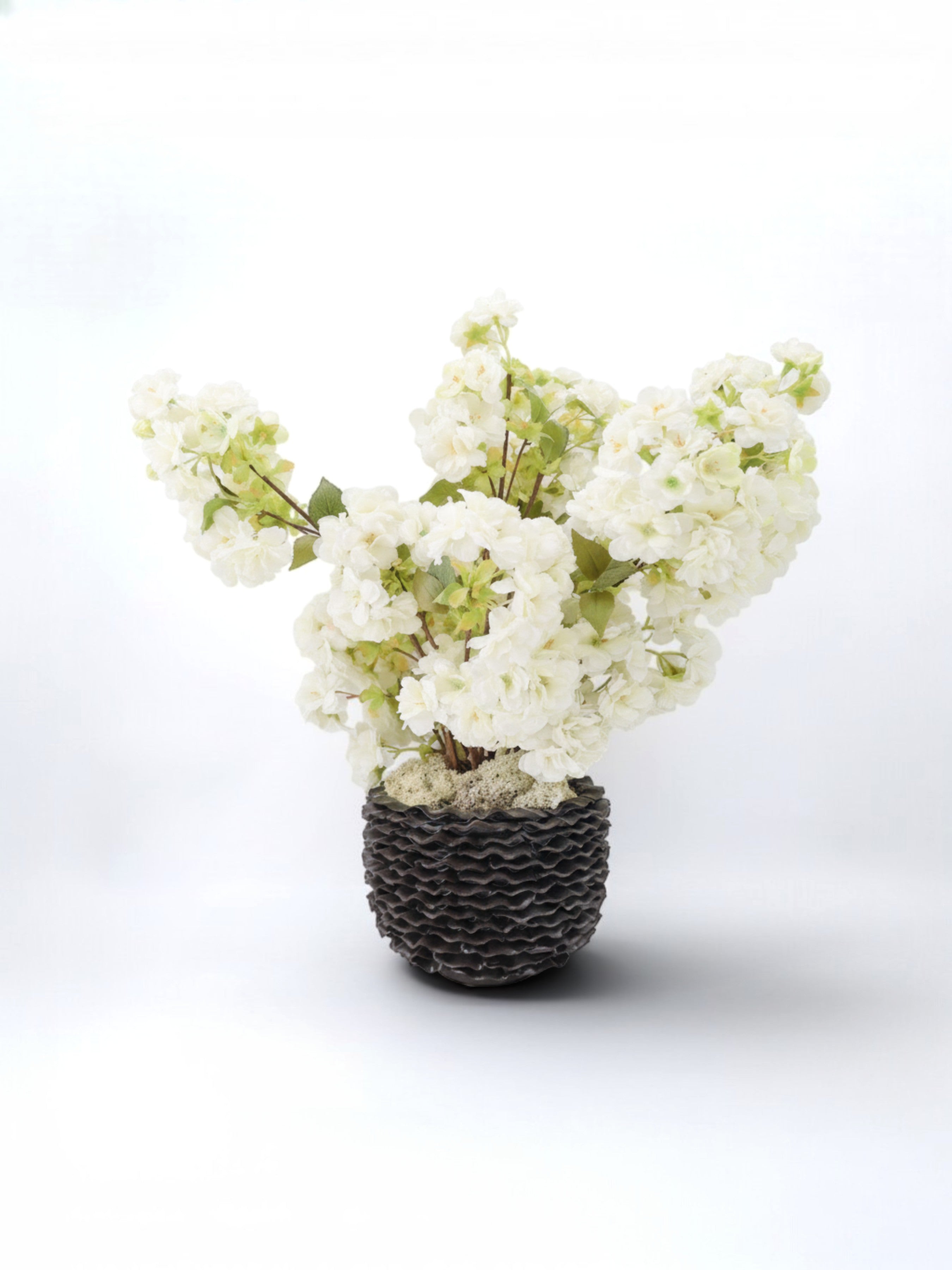 Sixty3 Styled artificial white cherry blossom arrangement in a dark textured pot with green foliage.