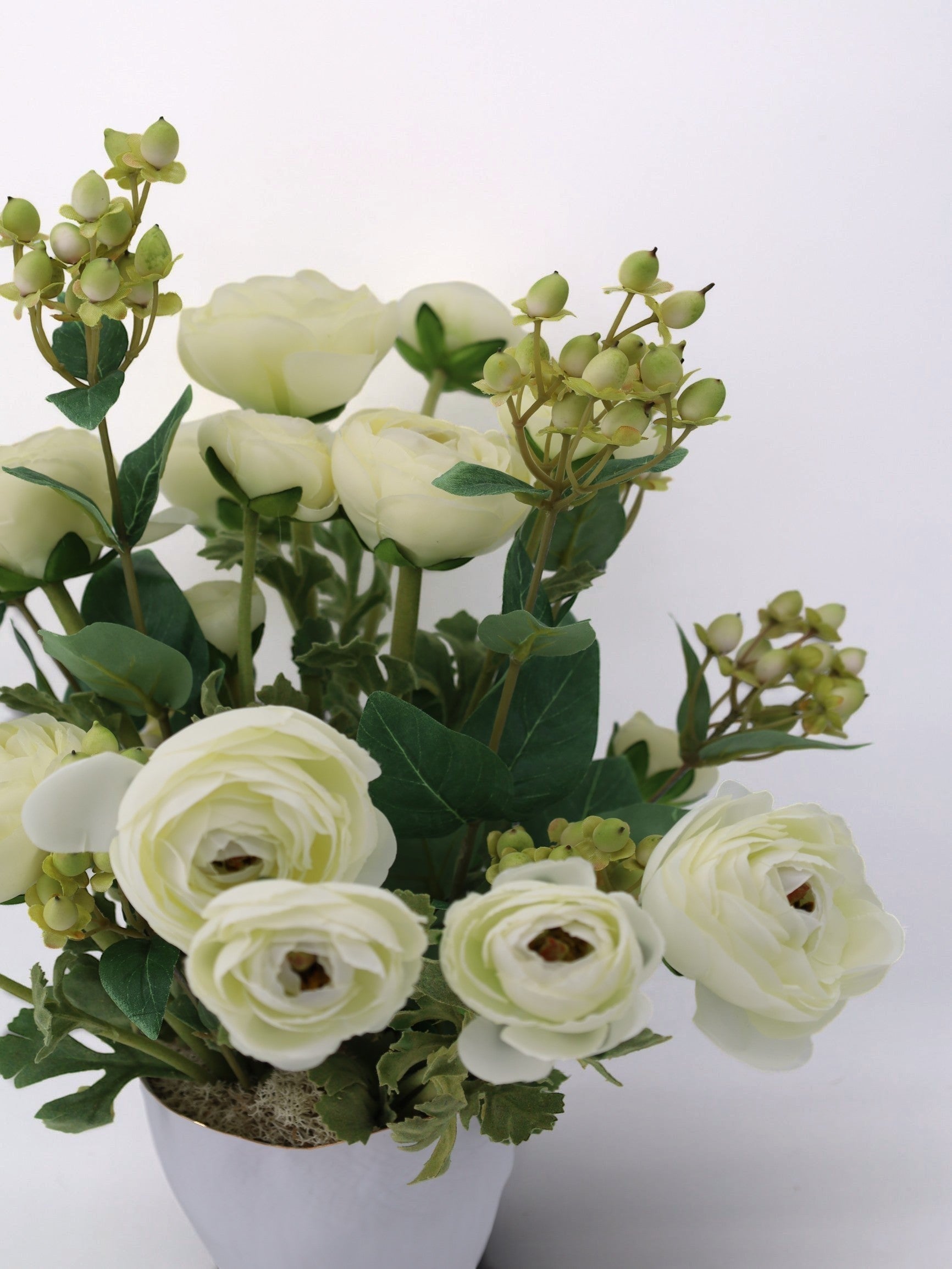 Sixty3 Styled cream ranunculus artificial floral arrangement in a white pot with green foliage and berries.